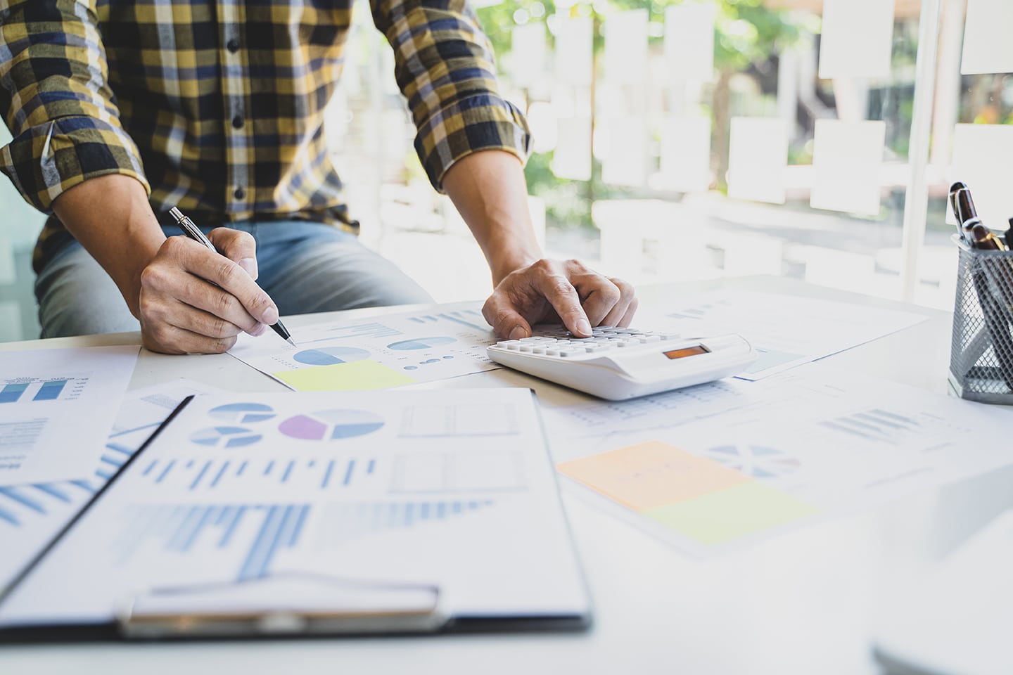 Man standing over table looking at spreadsheets and typing in a calculator