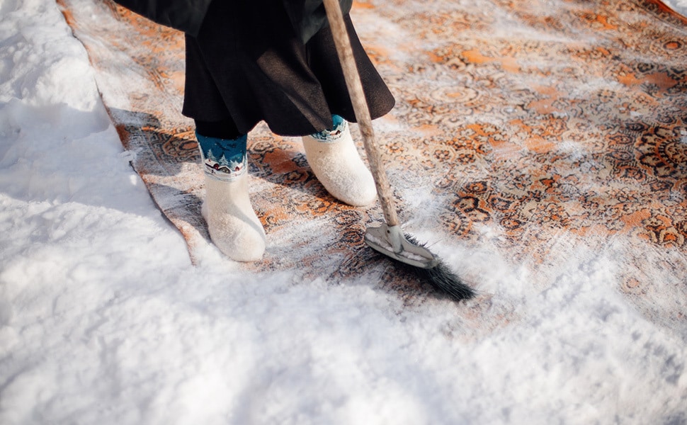 Person sweeping snow off a rug