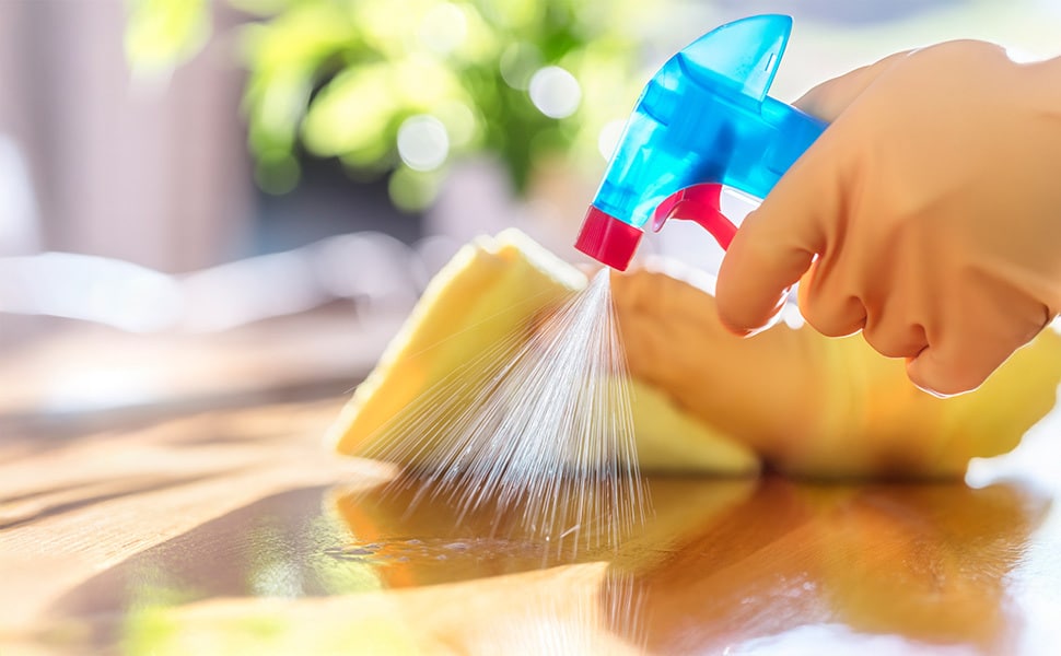 Hand spraying outdoor wood surface with cleaning spray and sponge