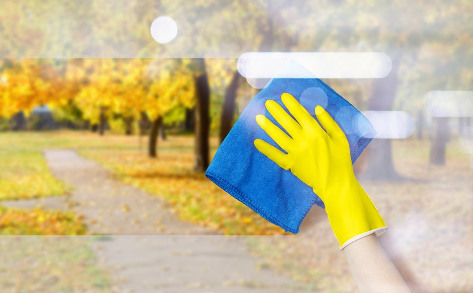 A gloved hand wipes the fog off of a window where you can see trees and fall colors outside.