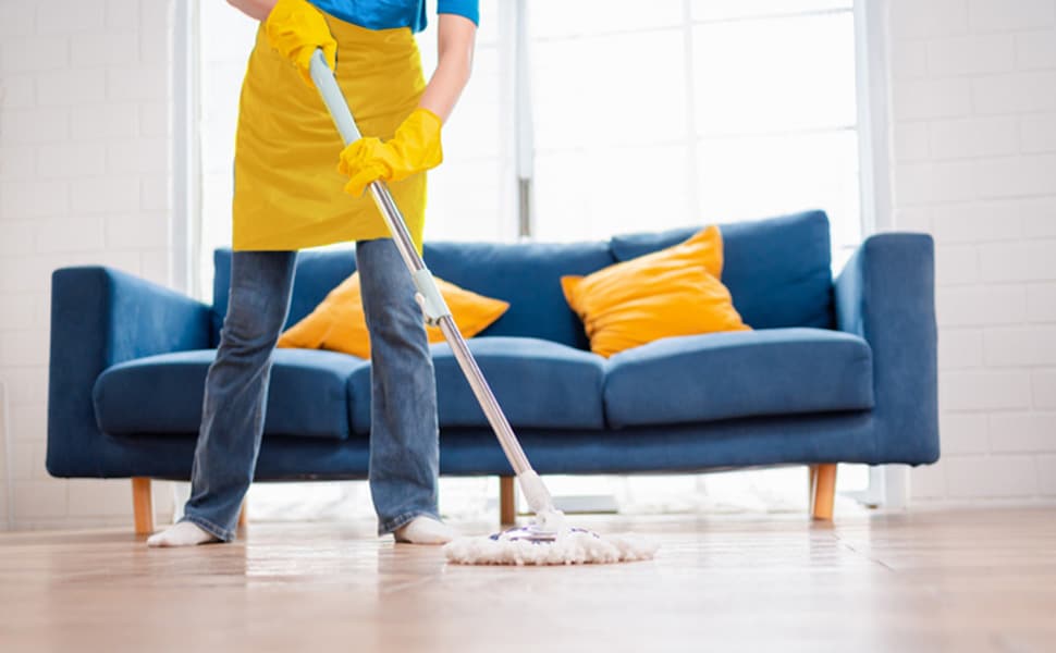 A person in a Maids cleaning outfit mops the living room in front of a blue couch.
