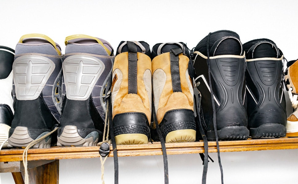 Three pairs of ski boots are lined up in a row on a closet shelf.